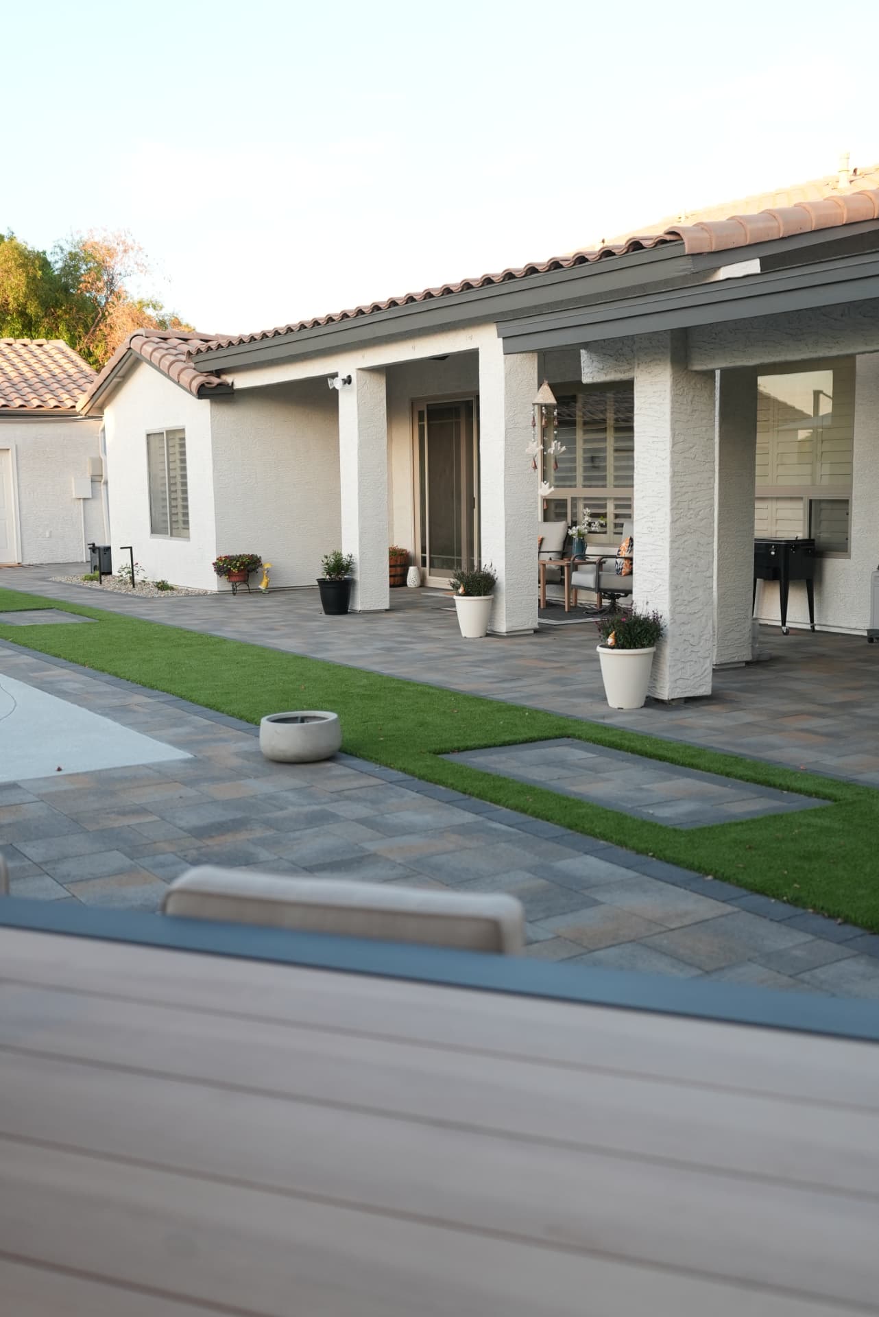 Paver patio with green turf inlay bands running along a white house