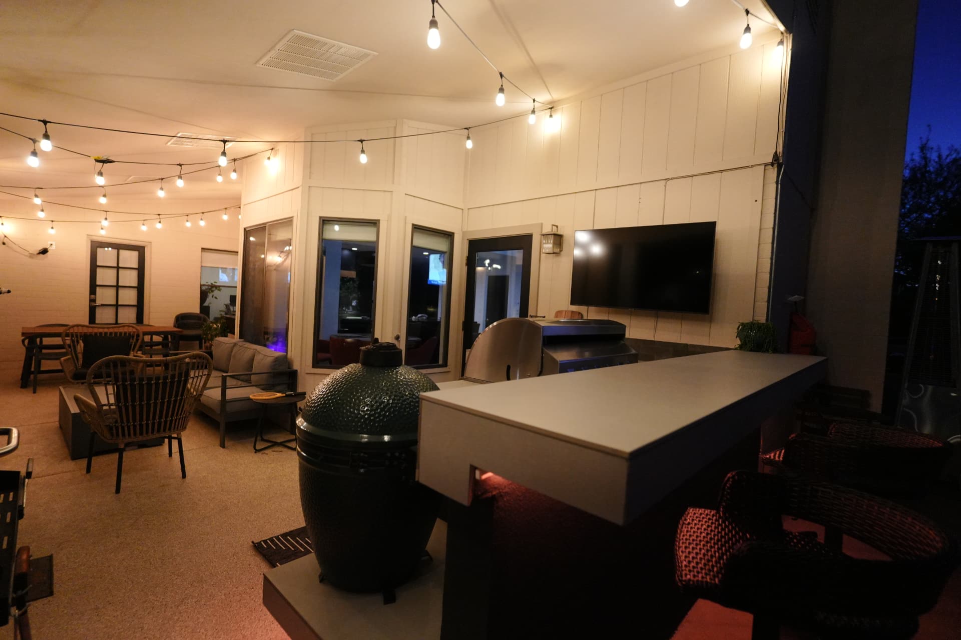 Outdoor kitchen at night with TV, kamado grill and string lighting