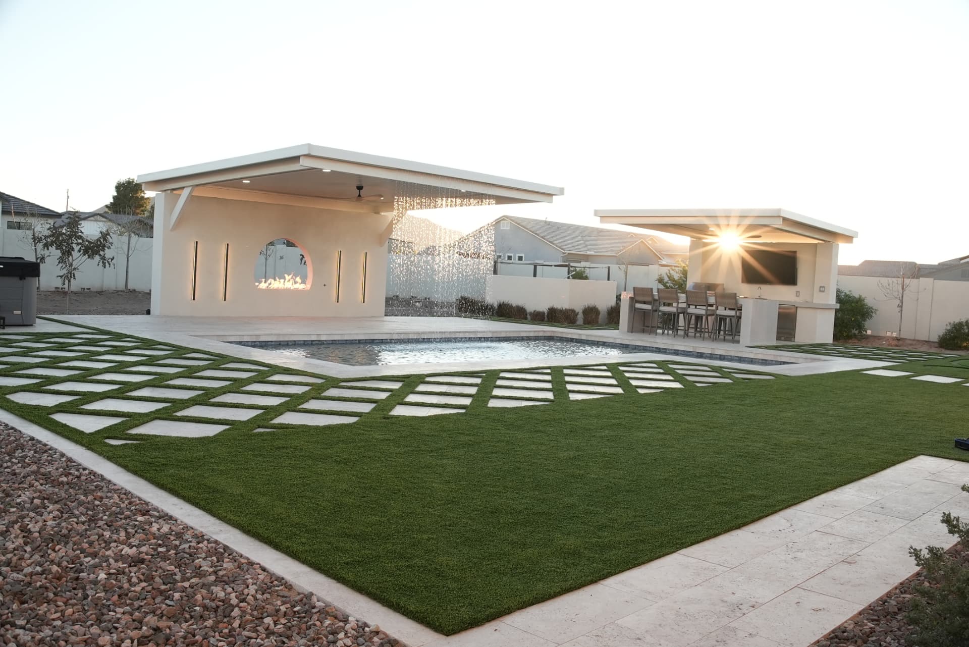 Backyard with two flat-roof pavilions, pool and large turf lawn at sunset