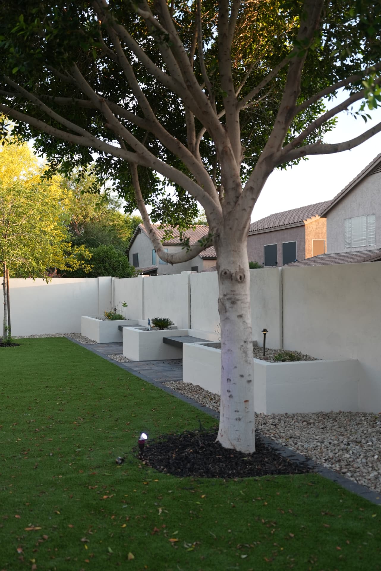White stucco planters with floating bench seats along a wall beside turf