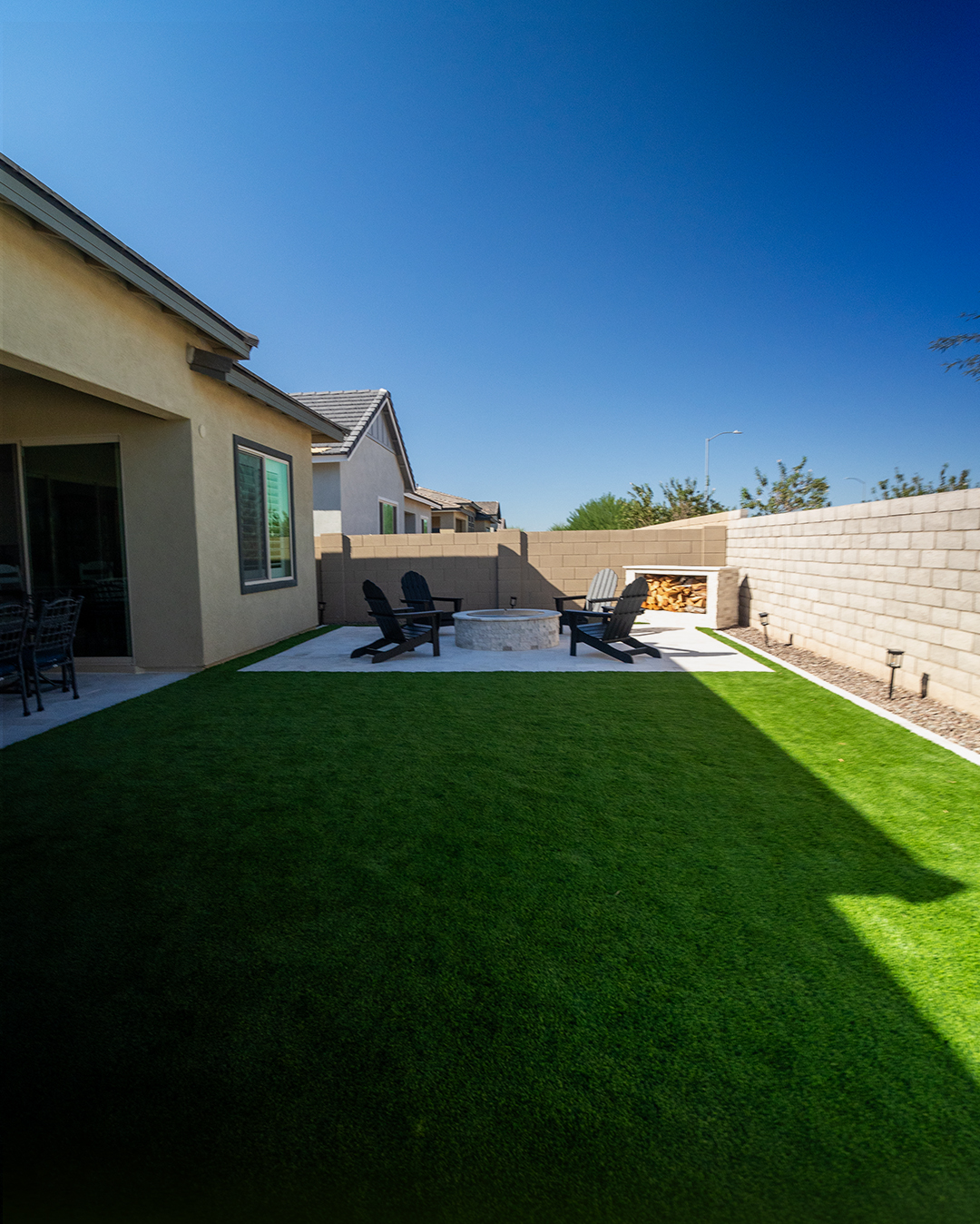 Backyard with travertine fire pit patio, turf lawn and path lighting at dusk
