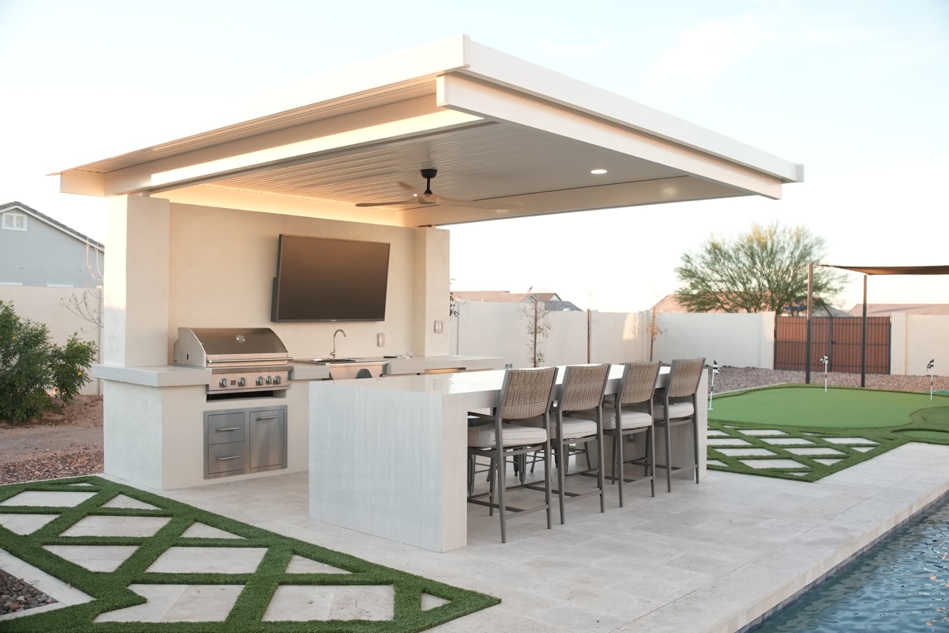 Outdoor kitchen with grill, bar seating and TV under a flat-roof cabana