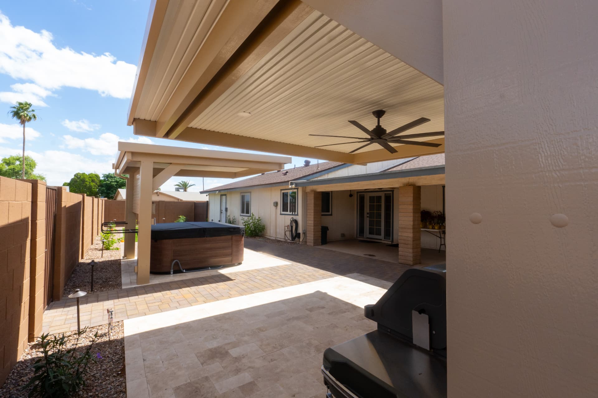Hot tub under a covered patio beside a travertine deck and paver path