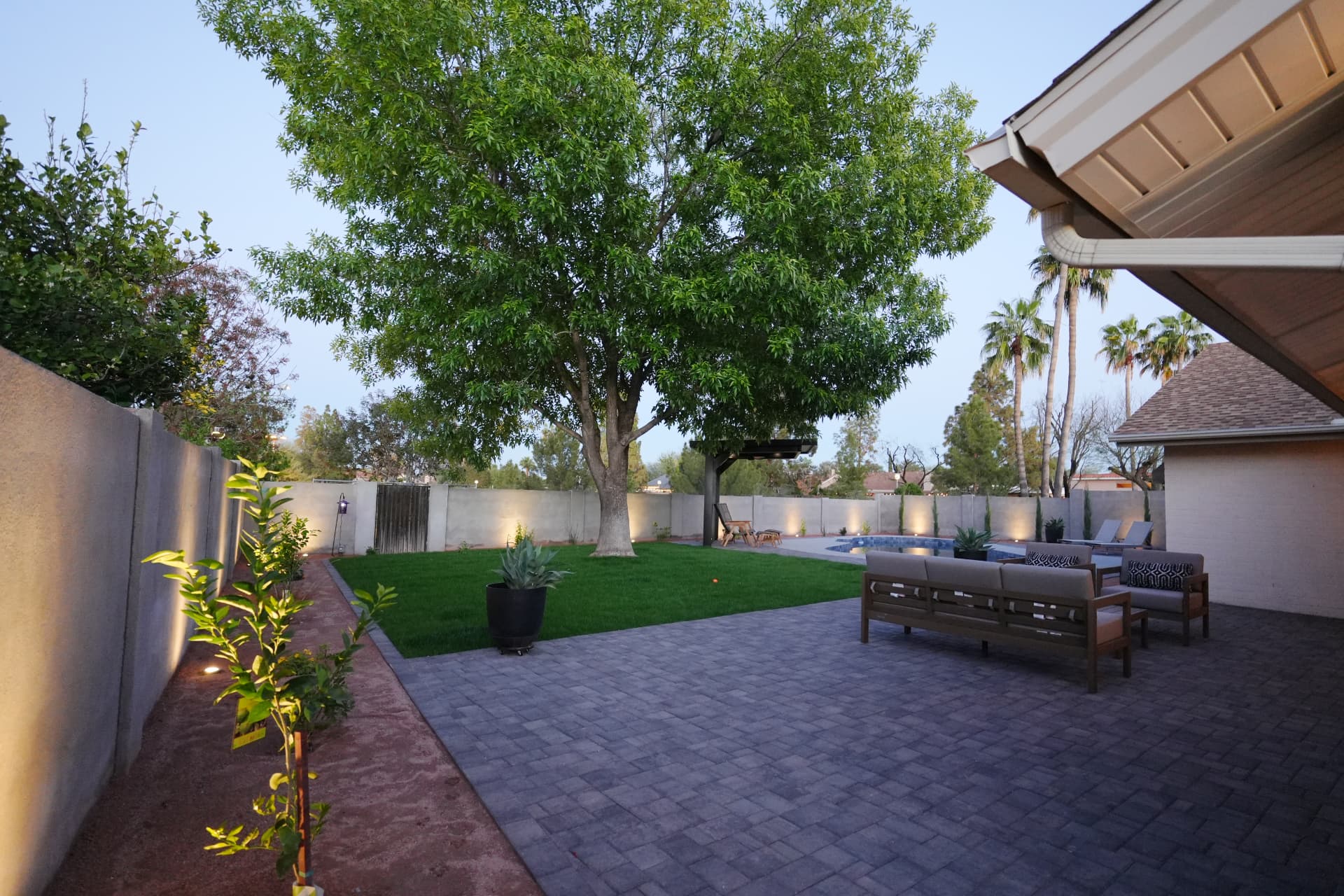 Backyard paver patio with lounge furniture, turf lawn and mature shade tree