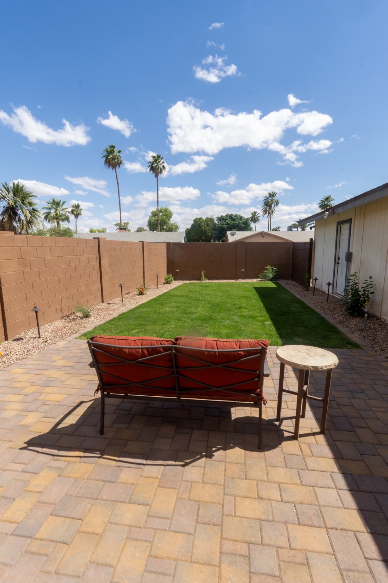 Paver patio with lounge chairs facing a striped artificial turf lawn