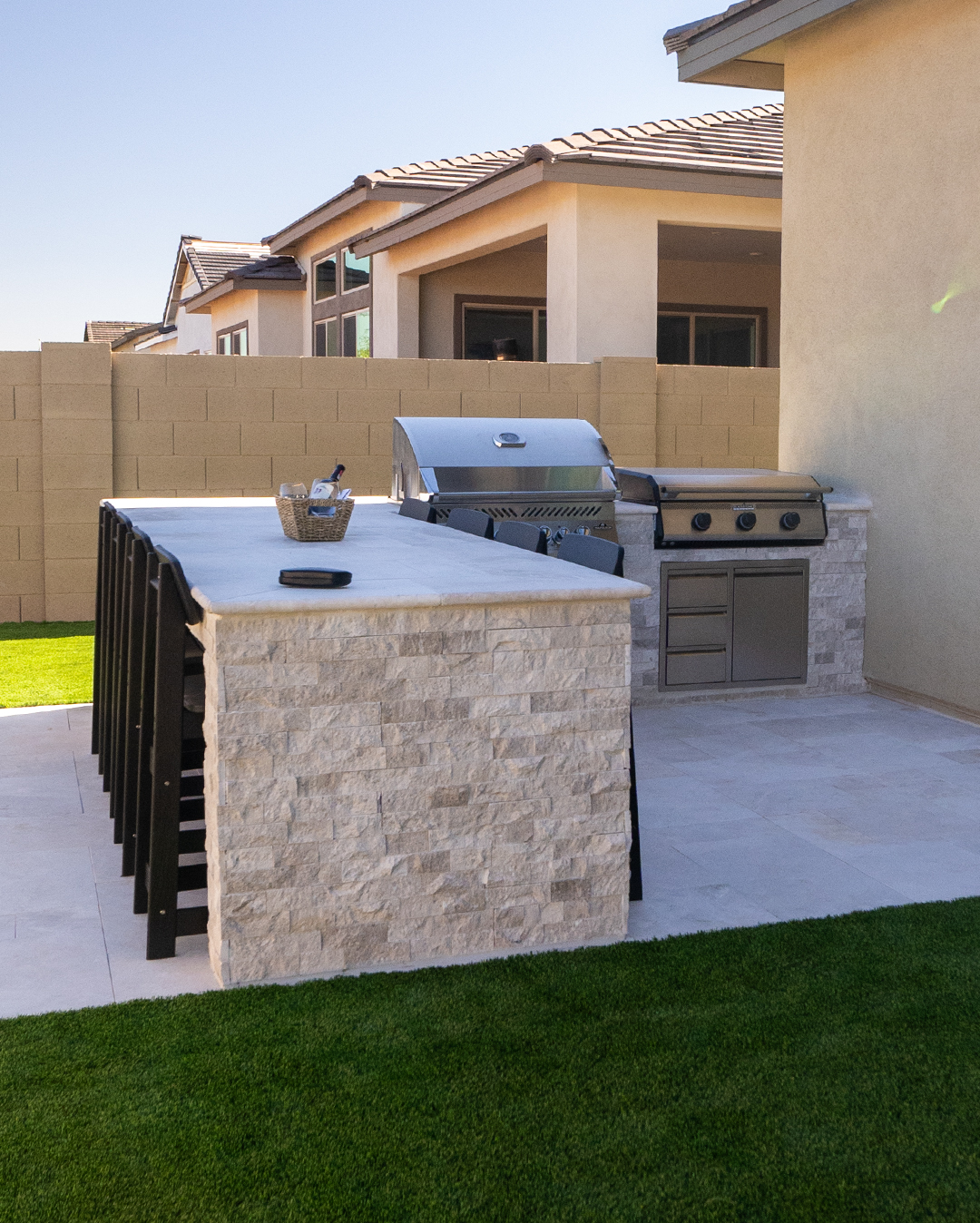 Stone outdoor kitchen bar with stools seen from the artificial turf lawn