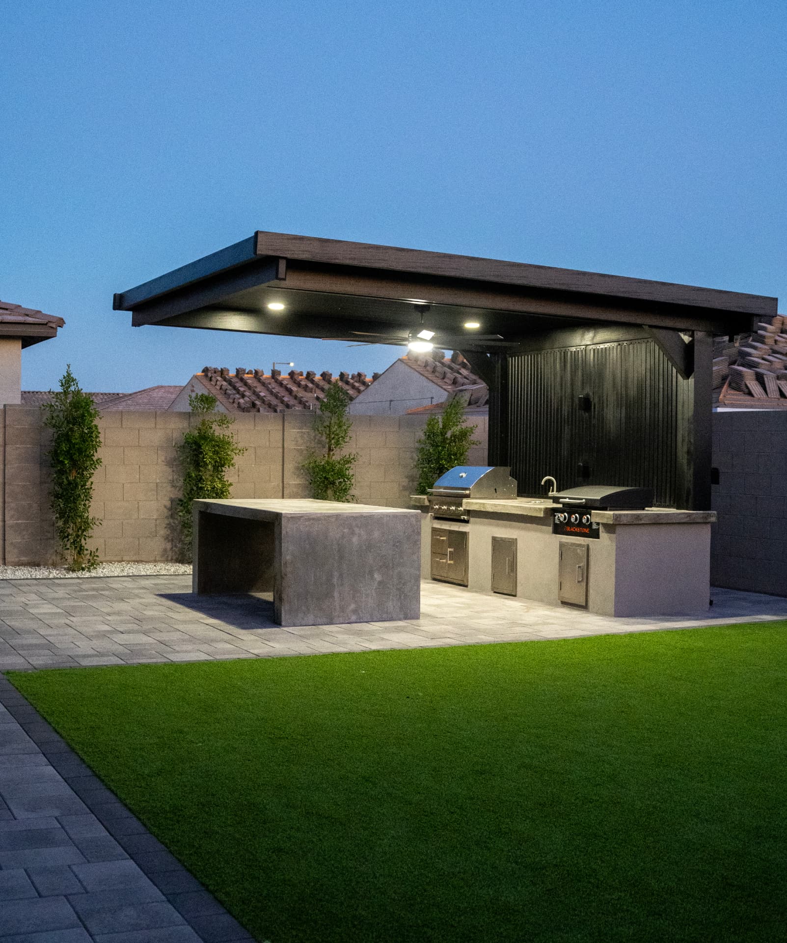 Backyard at dusk with pergola, outdoor kitchen, paver patio and turf lawn