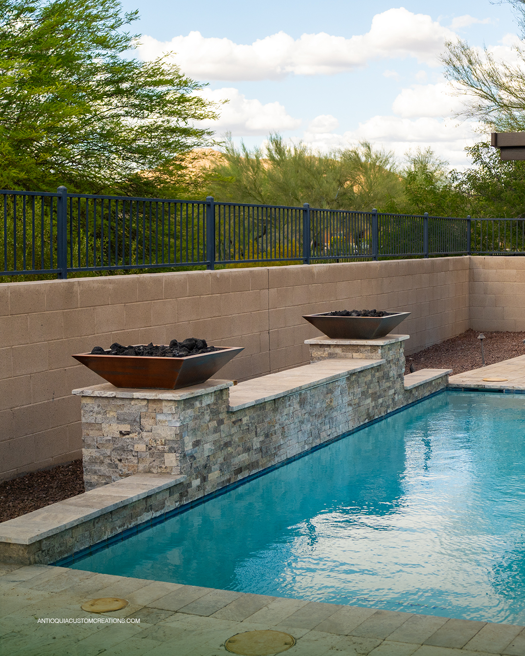 Two copper fire bowls on stone pedestals along a raised pool wall