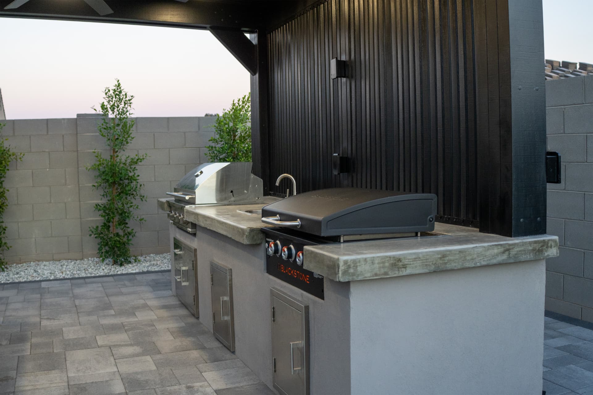 Outdoor kitchen with stainless grill, griddle and sink under a slat wall
